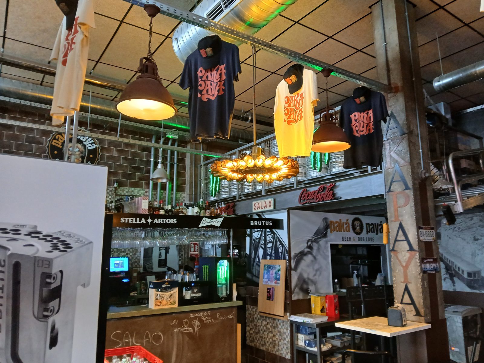 Camisetas y gorras PakáPayá colgadas en la barra del bar