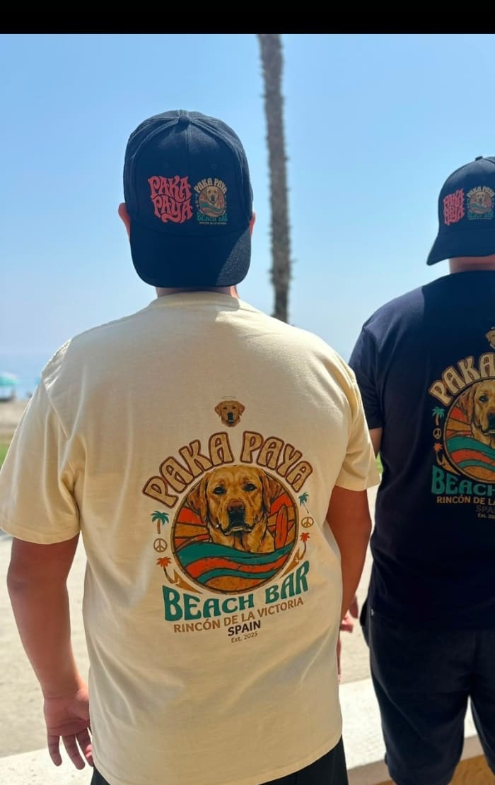 Dos amigos paseando con camiseta y gorra PakáPayá frente al mar